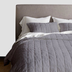 Gray quilted comforter and pillows on a bed with a gray headboard.