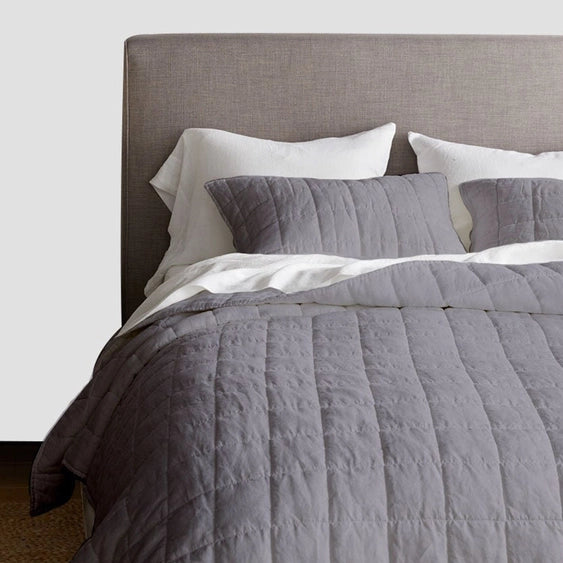 Gray quilted comforter and pillows on a bed with a gray headboard.