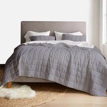 Gray quilted comforter on a bed with white pillows in a bedroom setting.