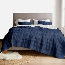 Bed with navy quilt and white pillows in a room with a rug and headboard.