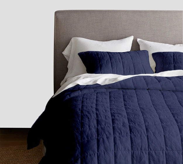 Bed with navy quilt and pillows against a gray headboard.