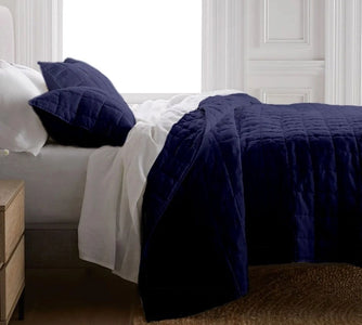 Navy blue quilted coverlet on a bed with white bedding in a bedroom setting.