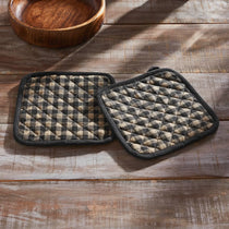 Two quilted cotton pot holders with a black and beige gingham pattern and dark gray trim, displayed on a rustic wooden table next to a wooden bowl.