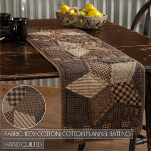 A rustic brown patchwork table runner with a quilted cotton fabric design, displayed on a dark wooden dining table. The runner features various patchwork patterns including plaid, check, and solid brown tones.