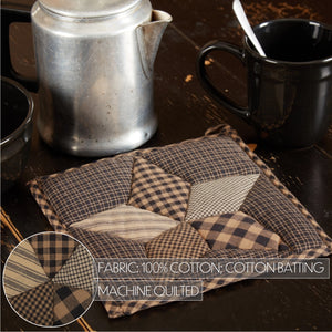 A handmade quilted cotton potholder with a patchwork design of plaid and checkered patterns in brown, beige, and black. The product is displayed on a dark wooden table next to a silver teapot and a black mug, with a circular inset showing the fabric textures and text overlay detailing the materials.