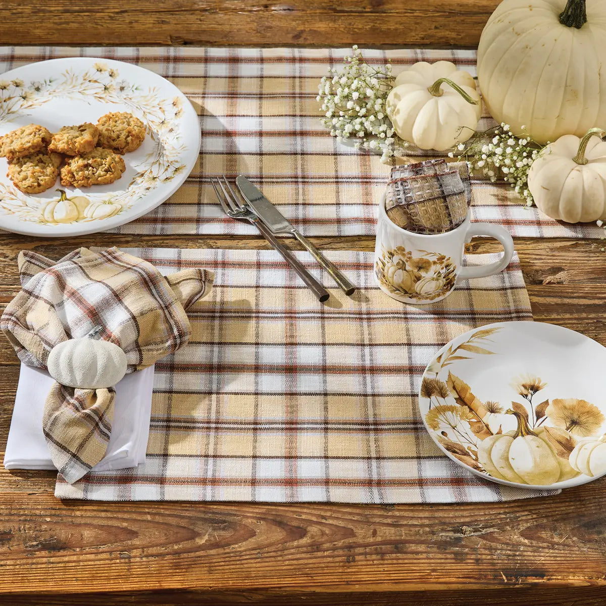Thanksgiving table setting with plaid placemats, pumpkins, and fall-themed plates.