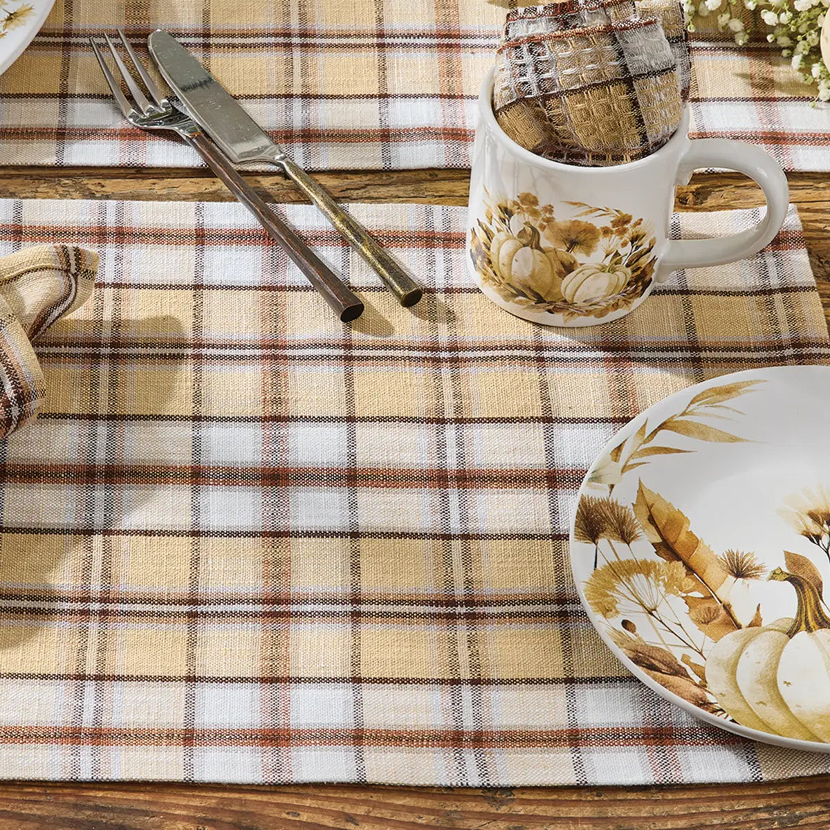 Plaid tablecloth with a cup, plate, and cutlery on a wooden surface