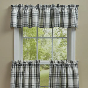 A set of plaid window curtains including a valance and two tier panels, shown hanging on a white window frame with a view of green trees outside.