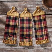 Three rustic kitchen towels with a red, black, and tan buffalo plaid pattern, featuring a small embroidered crow near the bottom and a tan cord loop with a button at the top, displayed on a weathered wood background.