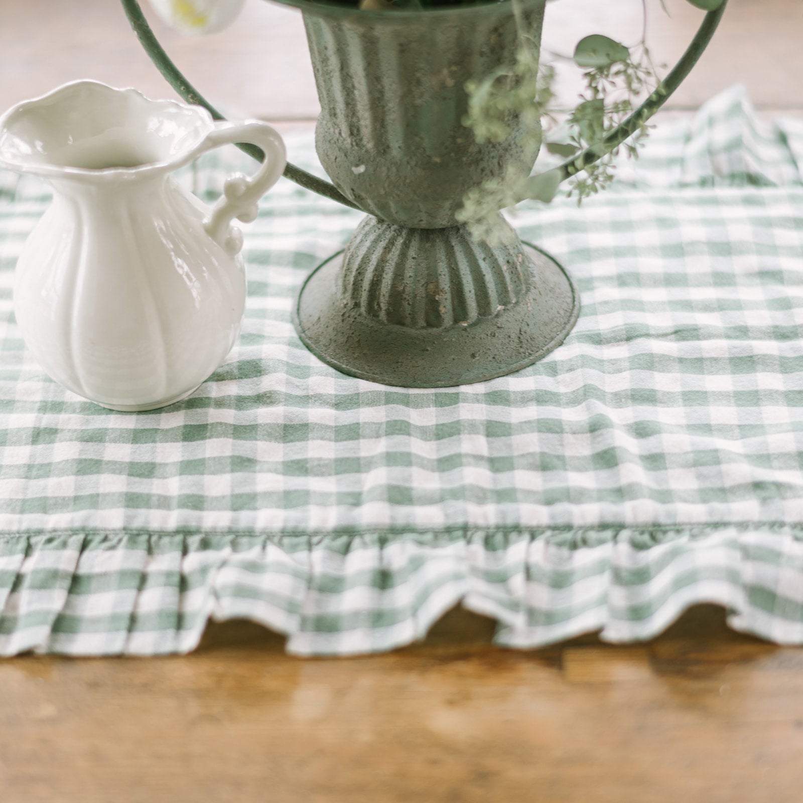 Green and white checkered tablecloth with a decorative vase and pitcher on a wooden surface.
