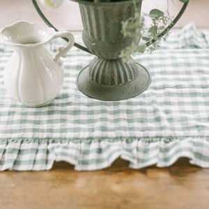 Green and white checkered tablecloth with a decorative vase and pitcher on a wooden surface.