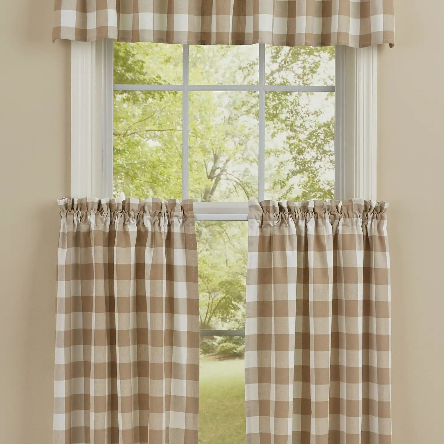 A set of window curtains featuring a brown and cream buffalo check gingham pattern, shown hanging on a white window frame with a matching valance, set against a beige wall with a green outdoor view.