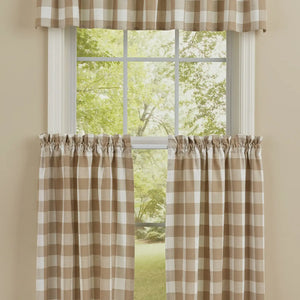 A set of window curtains featuring a brown and cream buffalo check gingham pattern, shown hanging on a white window frame with a matching valance, set against a beige wall with a green outdoor view.