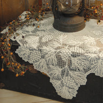 An off-white lace tablecloth with a detailed floral and leaf pattern draped over a dark wooden chest, styled with a vintage lantern and autumn berry garlands.